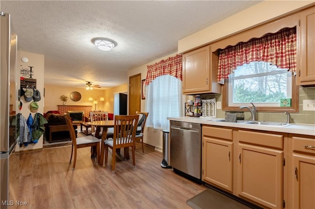 kitchen featuring light brown cabinetry, sink, light hardwood / wood-style flooring, stainless steel dishwasher, and a fireplace