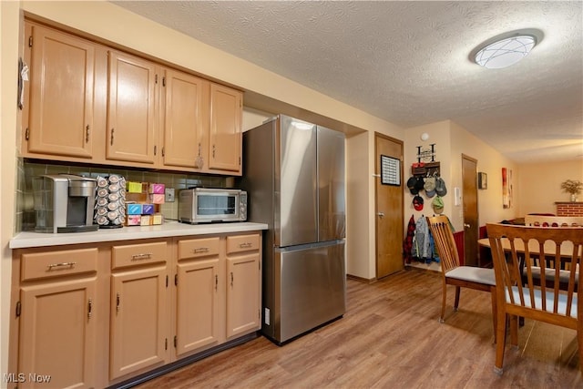 kitchen with light brown cabinetry, stainless steel refrigerator, decorative backsplash, a textured ceiling, and light wood-type flooring