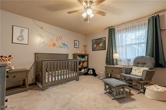 carpeted bedroom featuring a textured ceiling, a crib, and ceiling fan