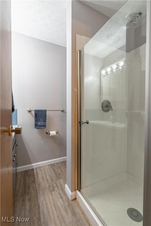 bathroom with wood-type flooring, a shower with door, and a textured ceiling