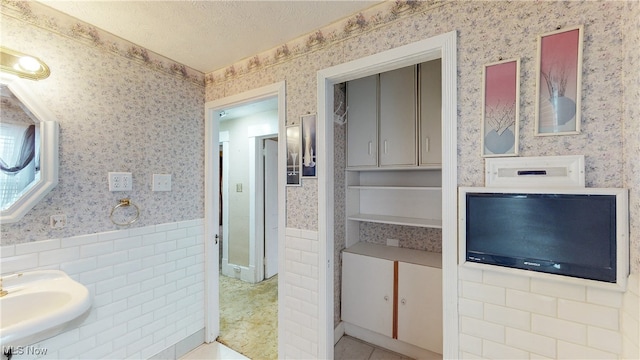 bathroom with tile patterned floors, sink, a textured ceiling, and tile walls