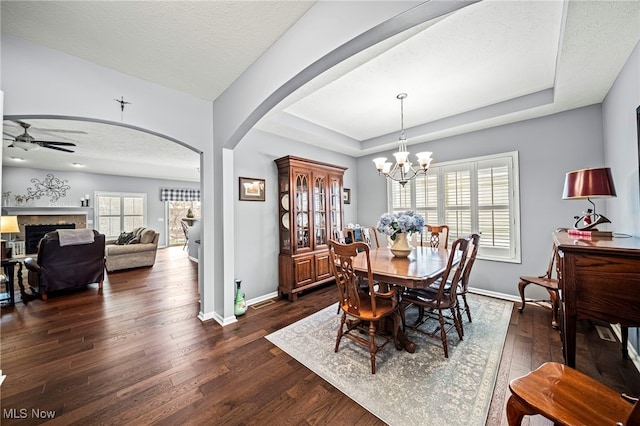 dining room featuring dark hardwood / wood-style floors, a raised ceiling, ceiling fan with notable chandelier, and a textured ceiling