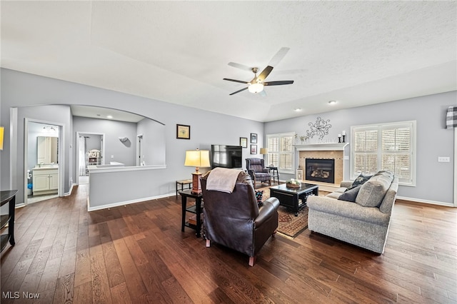 living room featuring dark hardwood / wood-style flooring, a textured ceiling, a tray ceiling, and ceiling fan