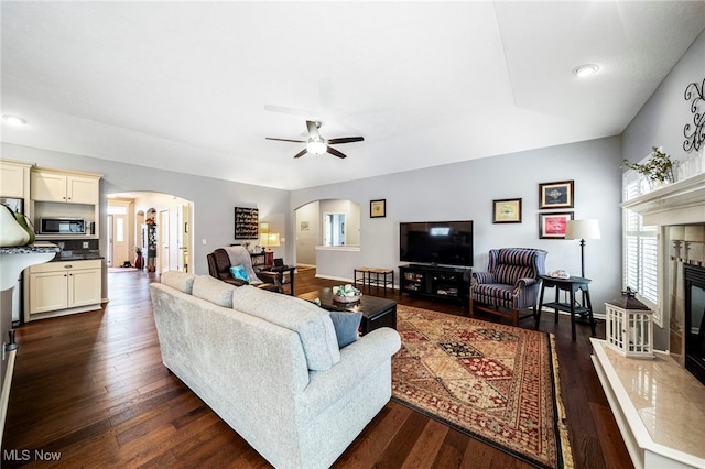 living room featuring a tiled fireplace, dark wood-type flooring, and ceiling fan