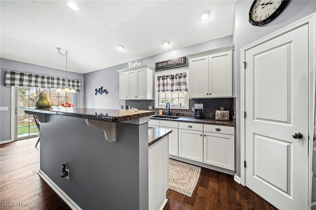 kitchen featuring white cabinetry, a kitchen bar, decorative light fixtures, and dark wood-type flooring