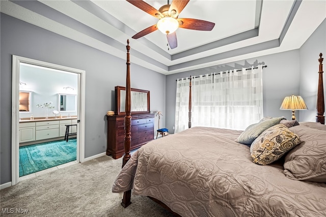 carpeted bedroom with a raised ceiling, ceiling fan, and ensuite bath