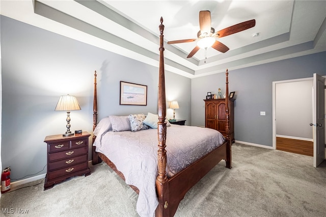 bedroom featuring a tray ceiling, light colored carpet, and ceiling fan