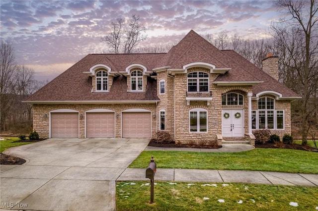 french country home featuring a garage, driveway, a yard, and roof with shingles