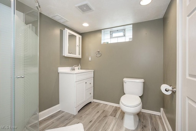 bathroom featuring wood-type flooring, walk in shower, vanity, and toilet