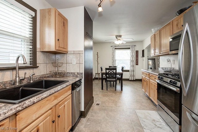 kitchen with sink, backsplash, light stone counters, ceiling fan, and stainless steel appliances