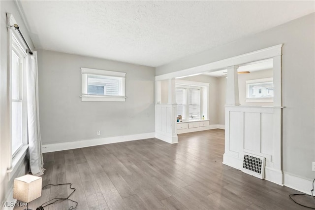 empty room featuring dark hardwood / wood-style flooring, a textured ceiling, and ornate columns