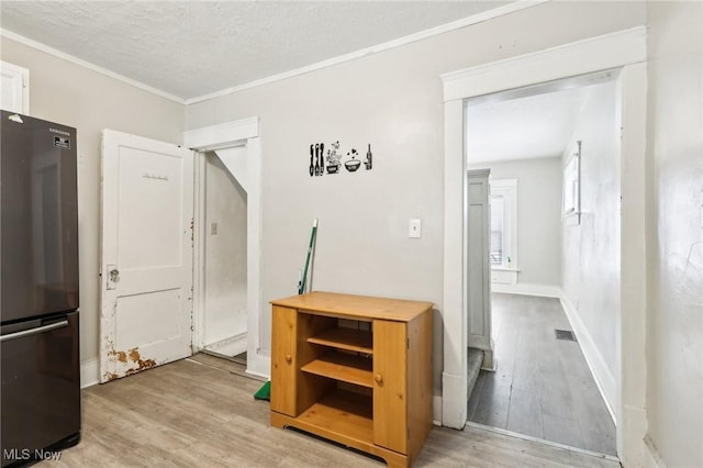 corridor featuring ornamental molding, a textured ceiling, and light hardwood / wood-style floors