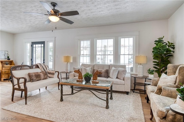 living room with ceiling fan, a textured ceiling, and light wood-type flooring