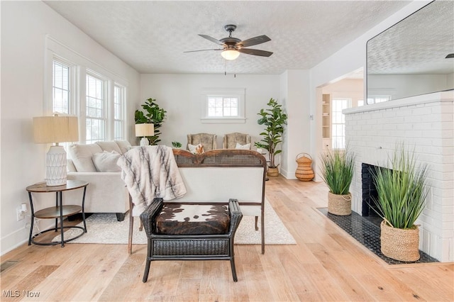 living room with a brick fireplace, a textured ceiling, and light wood-type flooring