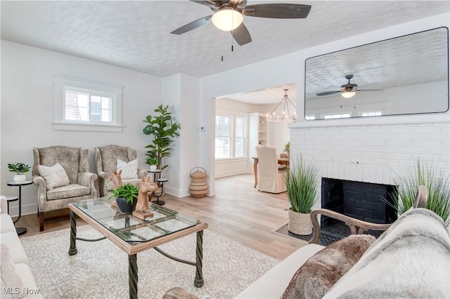 living room featuring ceiling fan, a textured ceiling, light wood-type flooring, and a fireplace