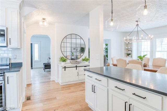 kitchen with decorative backsplash, white cabinets, light hardwood / wood-style floors, and decorative light fixtures