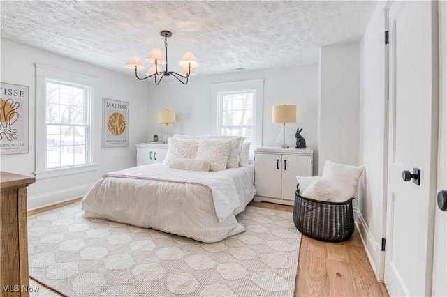 bedroom with an inviting chandelier, a textured ceiling, and light wood-type flooring