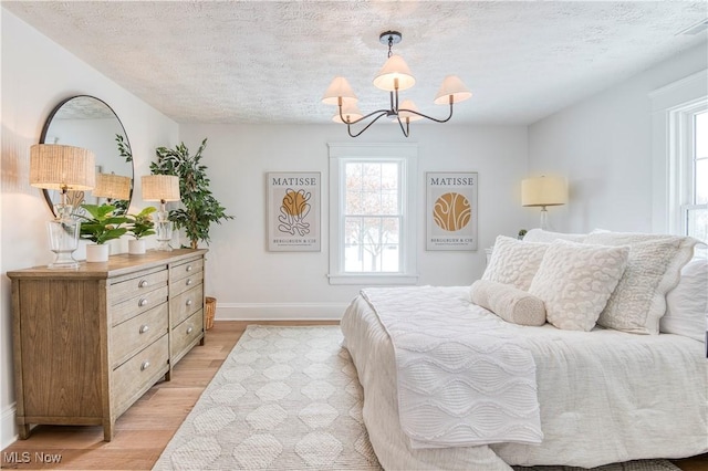 bedroom with a chandelier, a textured ceiling, and light wood-type flooring