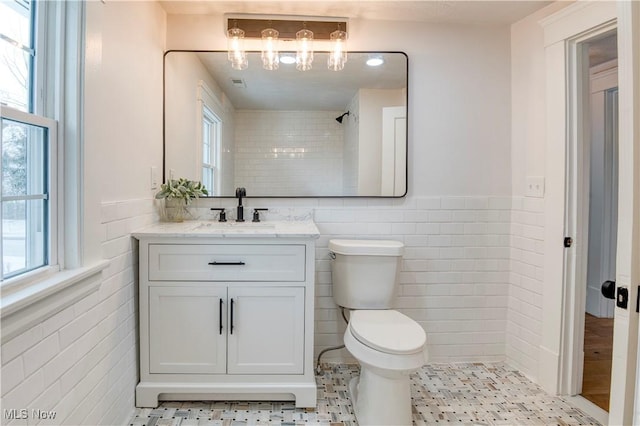 bathroom featuring vanity, toilet, tile walls, and a tile shower