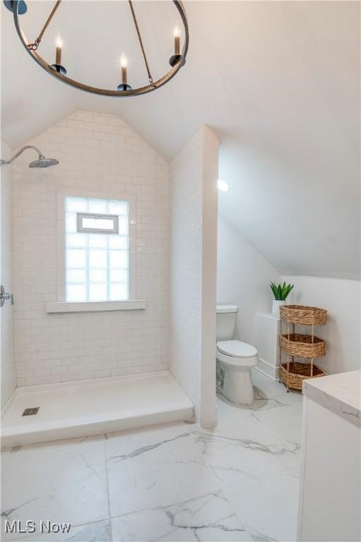 bathroom with tiled shower, vanity, toilet, and vaulted ceiling