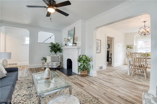 living room with wood-type flooring, ceiling fan with notable chandelier, and crown molding