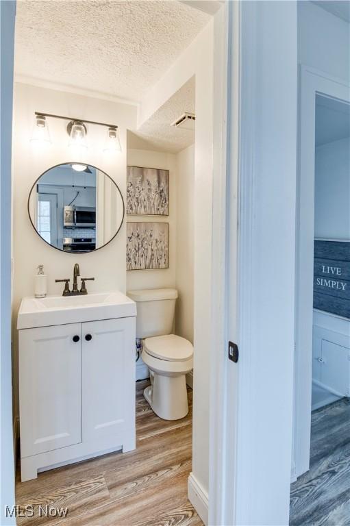 bathroom with hardwood / wood-style flooring, vanity, toilet, and a textured ceiling