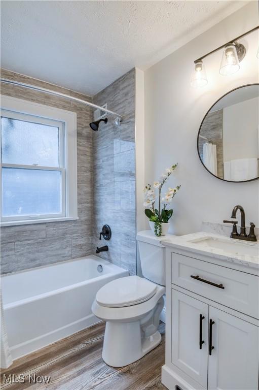 full bathroom featuring tiled shower / bath, hardwood / wood-style floors, vanity, toilet, and a textured ceiling