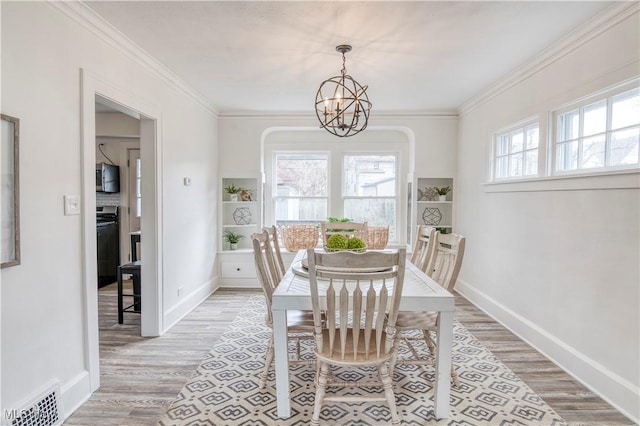 dining room featuring crown molding, a healthy amount of sunlight, a notable chandelier, and light hardwood / wood-style floors