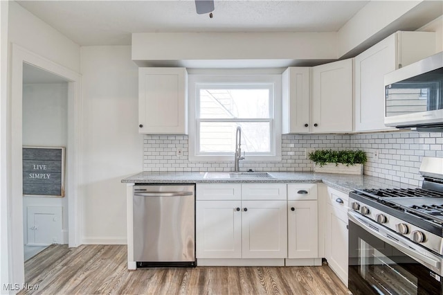 kitchen featuring stainless steel appliances, light stone countertops, sink, and white cabinets