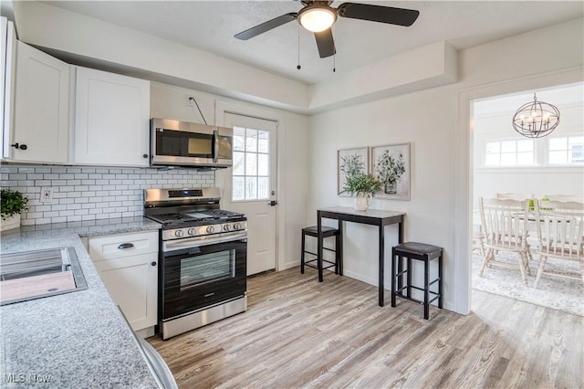 kitchen featuring white cabinetry, appliances with stainless steel finishes, light hardwood / wood-style floors, ceiling fan with notable chandelier, and backsplash