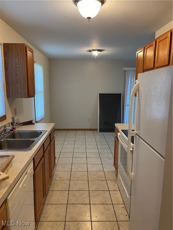 kitchen featuring sink, white appliances, light tile patterned floors, and a textured ceiling