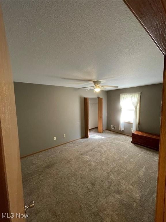 carpeted spare room featuring a textured ceiling and ceiling fan