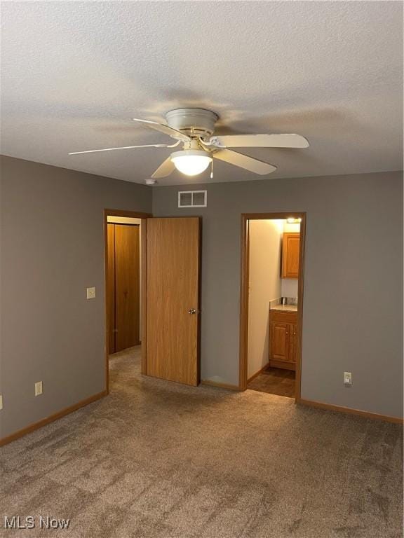 unfurnished bedroom featuring ceiling fan, light colored carpet, a textured ceiling, and ensuite bathroom