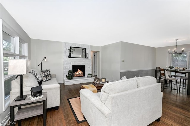 living room featuring a stone fireplace, dark hardwood / wood-style floors, and a chandelier