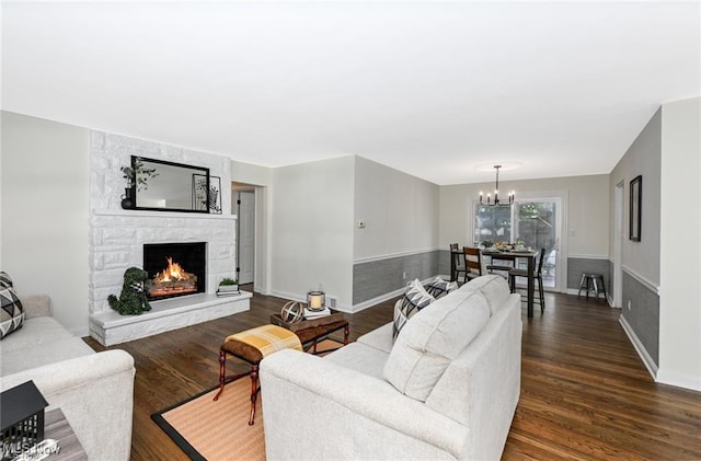 living room with a notable chandelier, a stone fireplace, and dark wood-type flooring