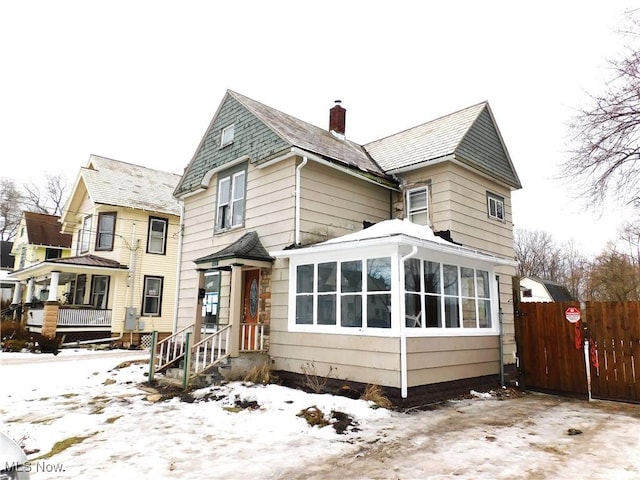 snow covered back of property with a sunroom