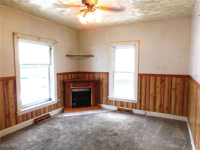 unfurnished living room with ornamental molding, light carpet, a wealth of natural light, and wood walls