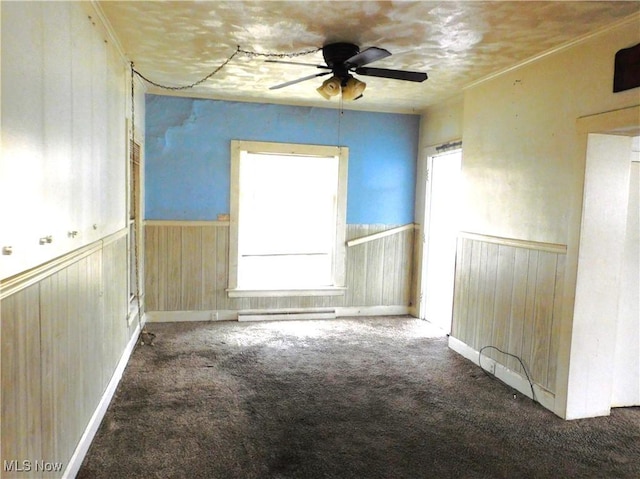 spare room featuring ceiling fan, carpet floors, a healthy amount of sunlight, and wood walls