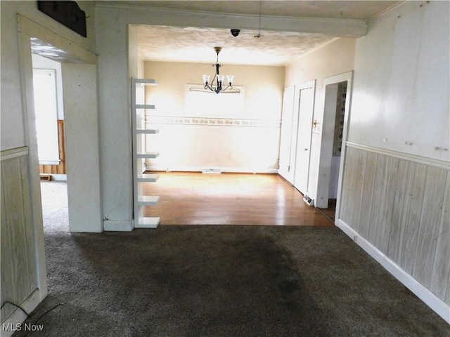 unfurnished dining area featuring wooden walls, a chandelier, and dark colored carpet