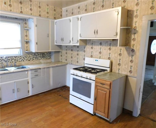 kitchen with sink, gas range gas stove, hardwood / wood-style flooring, decorative backsplash, and white cabinets