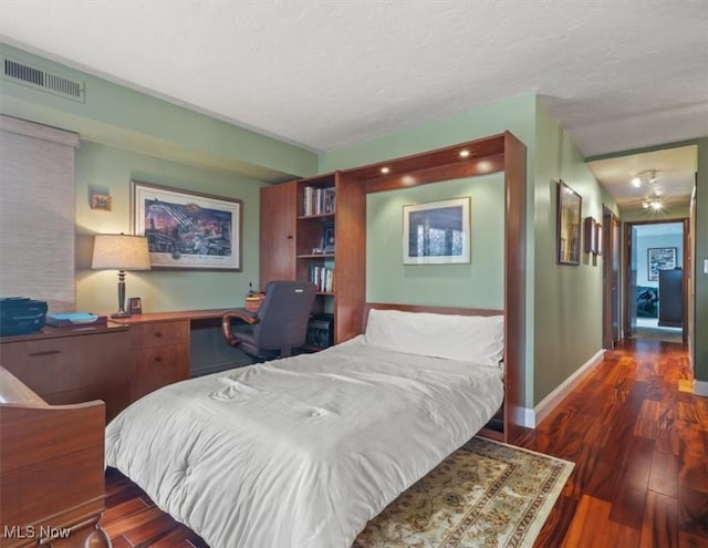 bedroom featuring dark hardwood / wood-style floors, built in desk, and a textured ceiling