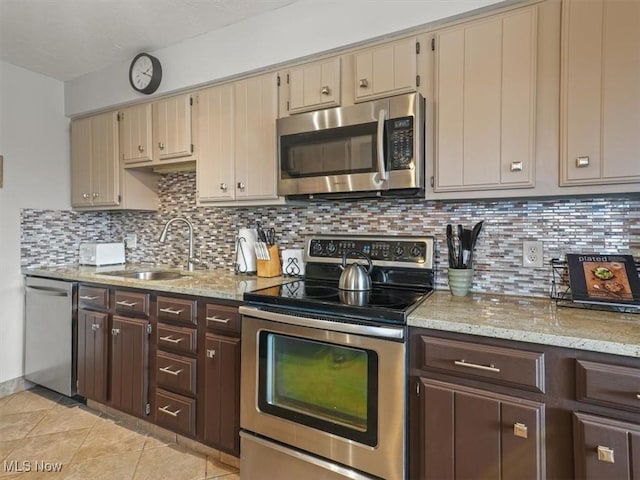 kitchen featuring light stone counters, sink, stainless steel appliances, and cream cabinetry