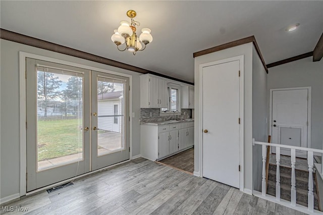 interior space with french doors, white cabinets, a chandelier, decorative backsplash, and light hardwood / wood-style flooring