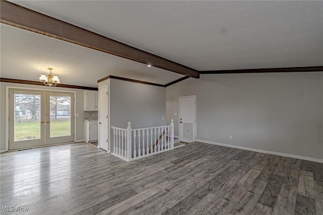 spare room featuring lofted ceiling with beams, a notable chandelier, light hardwood / wood-style floors, crown molding, and french doors