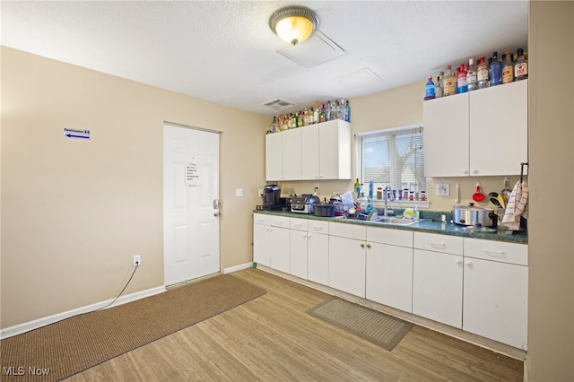 kitchen featuring white cabinetry, sink, light hardwood / wood-style floors, and a textured ceiling