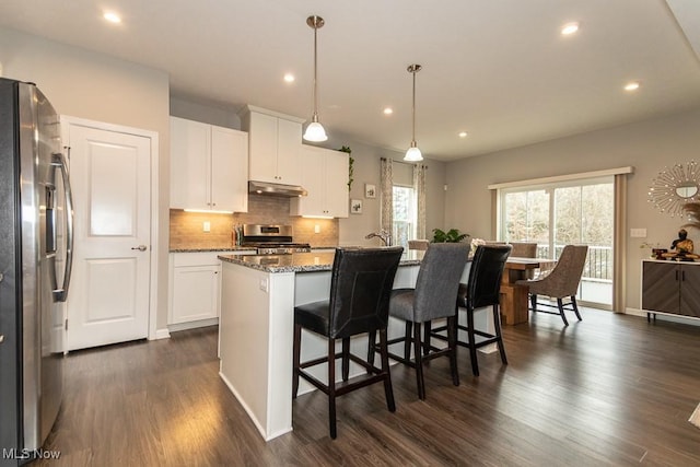 kitchen with appliances with stainless steel finishes, stone countertops, white cabinetry, an island with sink, and hanging light fixtures