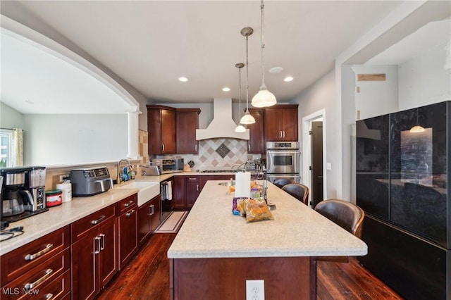 kitchen with decorative light fixtures, sink, a kitchen breakfast bar, custom exhaust hood, and a center island