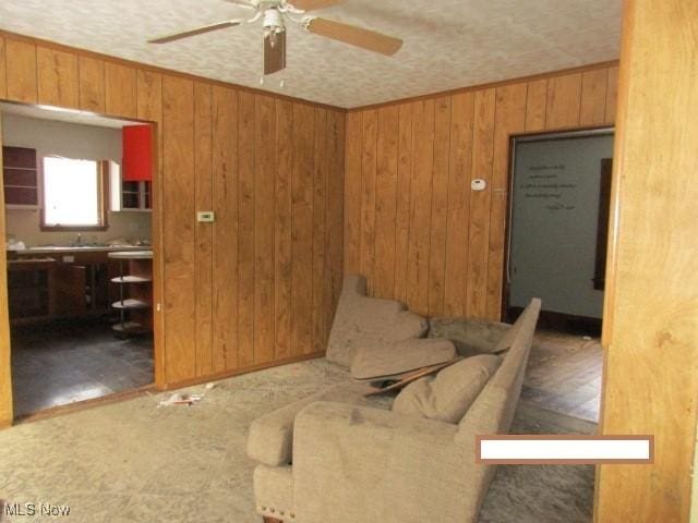 living room featuring ceiling fan, wood walls, and crown molding