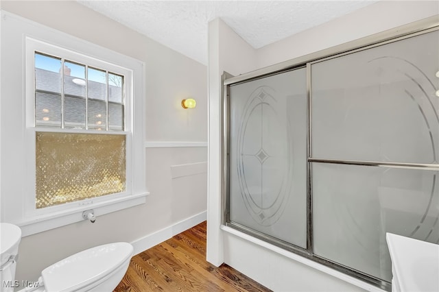 bathroom featuring wood-type flooring, combined bath / shower with glass door, a textured ceiling, and toilet