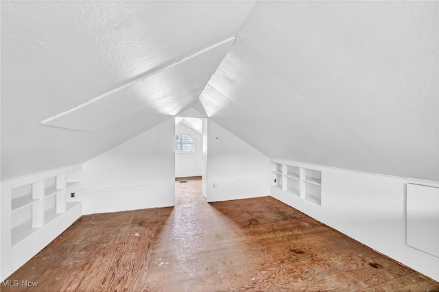 additional living space with vaulted ceiling, built in features, and a textured ceiling